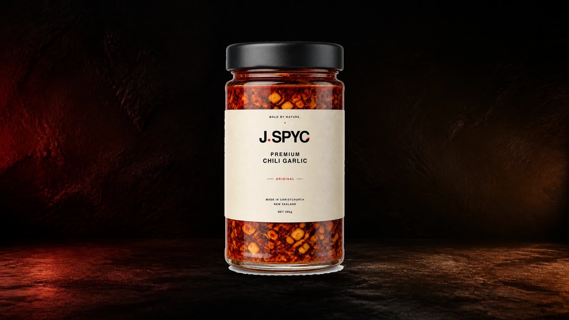 J.SPYC Original Premium Chili Garlic jar in a dark cinematic studio
